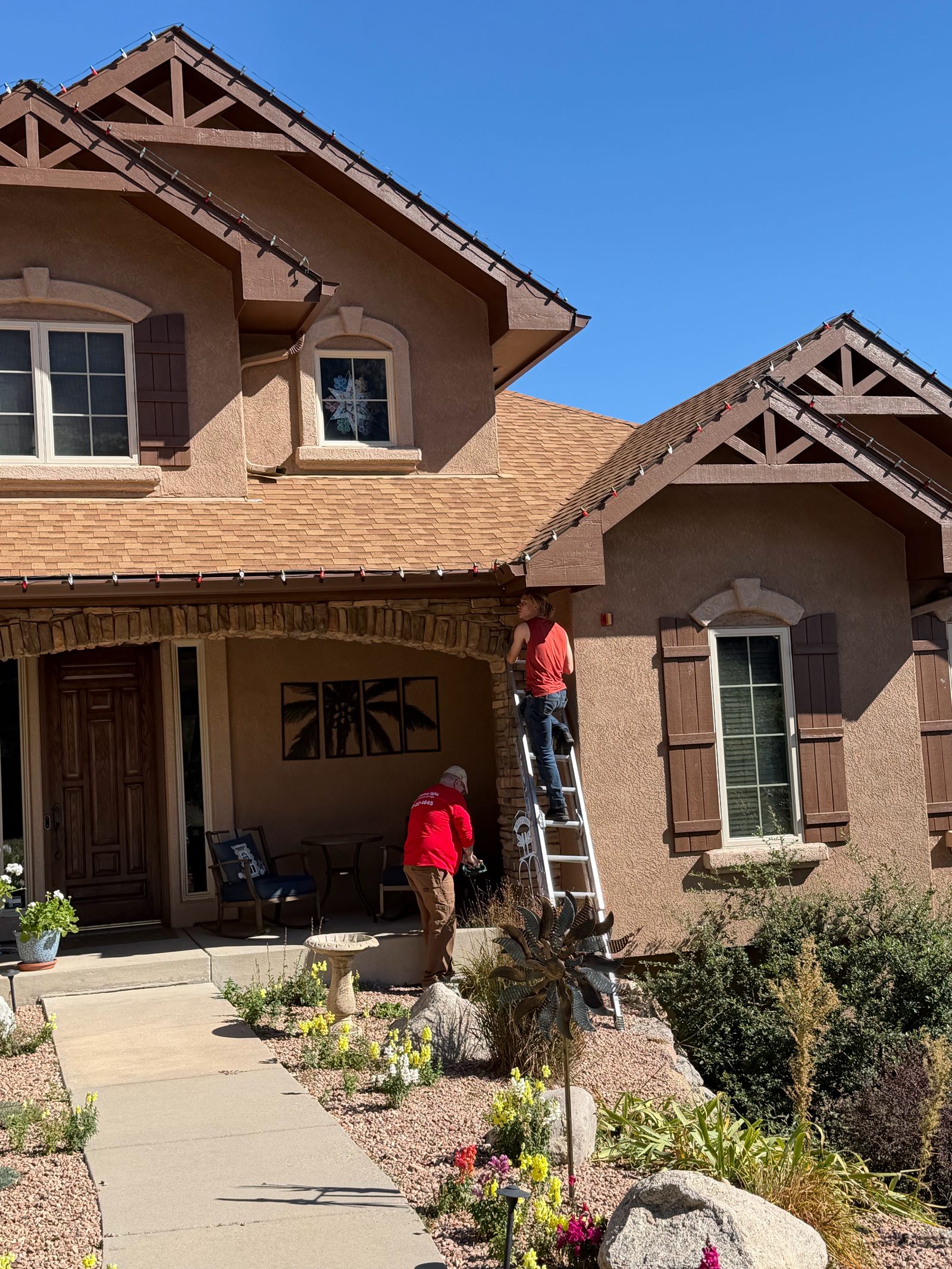 Christmas light installers on ladder hanging red Christmas lights on a Colorado Front Range home Christmas light installers on ladder hanging red Christmas lights on a Colorado Front Range home